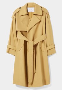 Manteau beige avec un large col, taille ceinturée, épaulettes et manches retournées. Fabriqué en tissu lisse, il comprend des poches latérales.