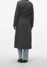 Grå lang frakke med bælte, lavet af tekstureret stof, med klassisk krave og lige pasform, båret over lyseblå jeans og sorte sko.