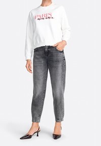 Weißer Hoodie mit "PARIS mon amie" in Rot, kombiniert mit hoch taillierten, schmal zulaufenden grauen Jeans und schwarzen Absatzmules. Strukturierter, lässiger Look.