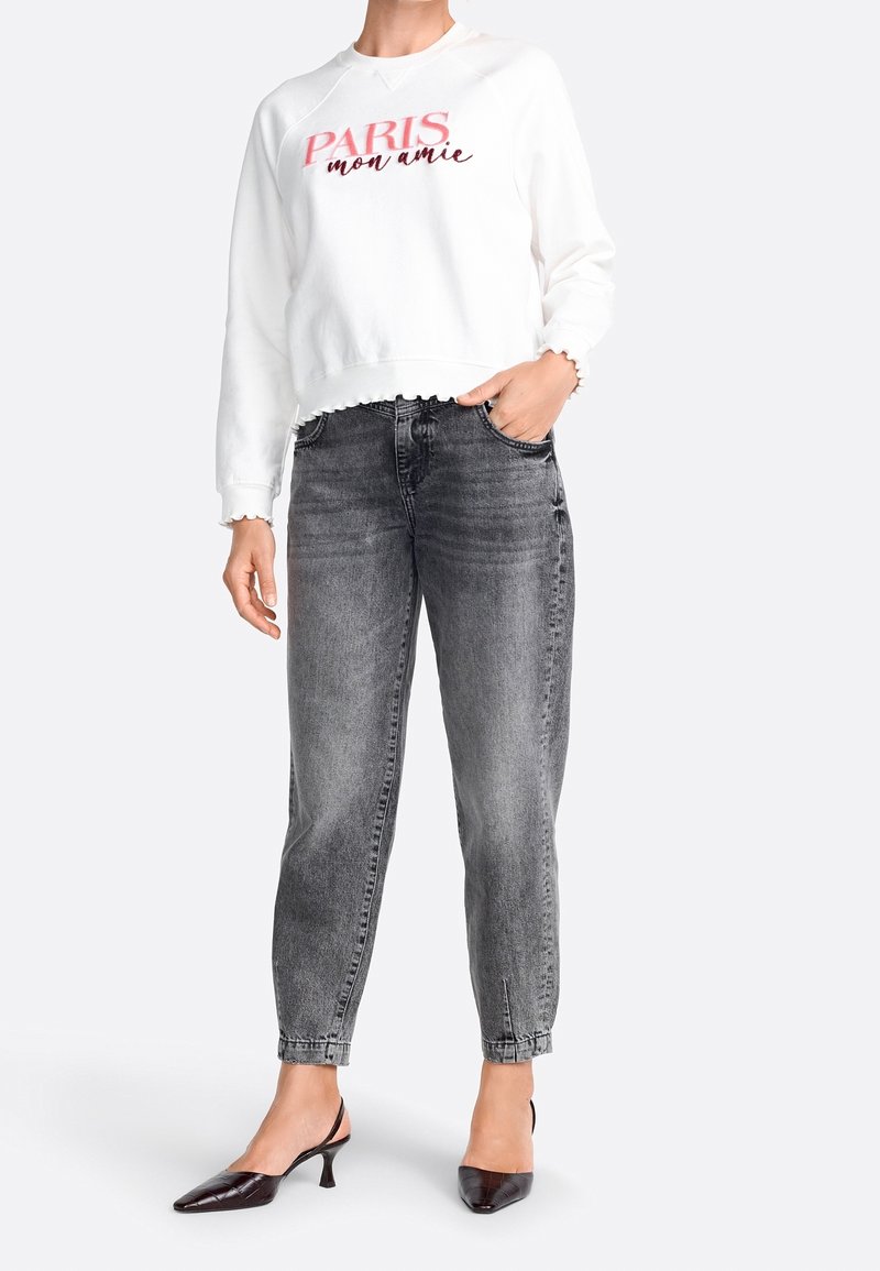Weißer Hoodie mit "PARIS mon amie" in Rot, kombiniert mit hoch taillierten, schmal zulaufenden grauen Jeans und schwarzen Absatzmules. Strukturierter, lässiger Look.