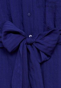 Abito in tessuto blu navy con un superficie testurizzata, chiusura con bottoni e un grande fiocco in vita, dotato di tasca.