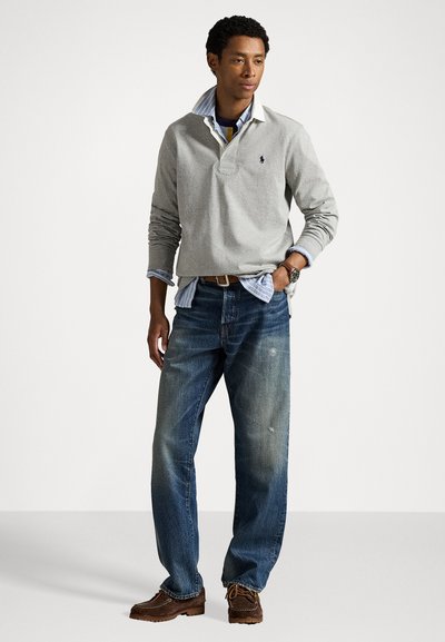 Lichtgrijze langemouwen polo met een kraag, gedragen over een blauwgestreept shirt, gecombineerd met blauwe denim spijkerbroeken en bruine veterschoenen.