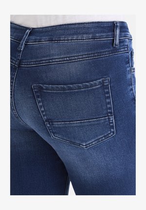 Dunkelblaue Denim-Jeans mit einer taillierten Passform und einer einzelnen Gesäßtasche. Der Stoff zeigt eine dezente Textur mit einem leichten Verwaschungseffekt.