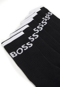 Calcetines de algodón negros con textura acanalada, rematados con una banda blanca y el logo "BOSS" en letras blancas a lo largo del lado.
