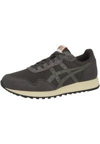 Zapatillas de deporte en gris oscuro con una parte superior de malla y ante. Presentan detalles en color verde y una suela color crema. Atadas con cordones marrones planos.