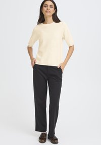 Kreem värvi lühikeste varrukatega sviiter ümmarguse kaelusega, koos mustade kohandatud pükstega. Pruunid jalanõud on tekstuurse disainiga.