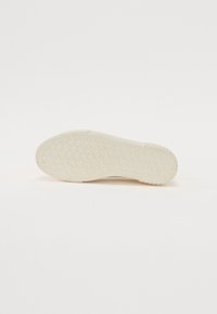 Semelle de chaussure en caoutchouc de couleur blanc cassé avec un motif texturé et géométrique présentant des triangles entrelacés et un talon arrondi.