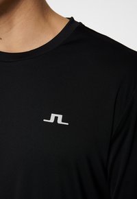 Svart kortärmad t-shirt i glatt material med en liten vit logotyp på bröstet, rund halsringning och en avslappnad passform.