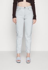 Jeans azzurri chiari a vita alta con un taglio aderente e risvolti, abbinati a sandali aperti blu decorati con motivi floreali.