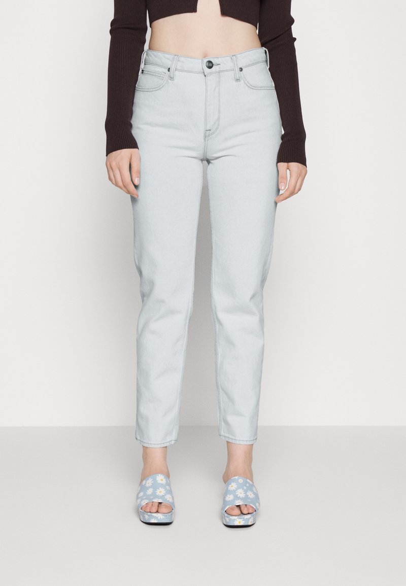 Jeans azzurri chiari a vita alta con un taglio aderente e risvolti, abbinati a sandali aperti blu decorati con motivi floreali.