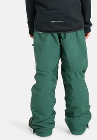 Groene sneeuwbroeken met een relaxed fit, voorzien van ritsen bij de enkels en een subtiele textuur, gecombineerd met een zwart shirt met lange mouwen.