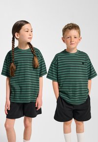 Gröna randiga T-shirts av bomull med korta ärmar och rund halsringning, tillsammans med svarta shorts. T-shirtsen har en välkänd logotyp.