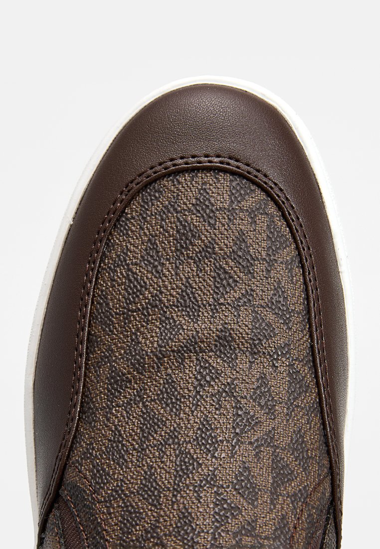 Bout de sneaker marron avec un tissu texturé présentant un motif géométrique et une finition en cuir lisse, souligné par une semelle en caoutchouc blanche.