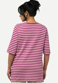Top de manga corta a rayas en rosa y crema, con un corte holgado y escote redondo. Tejido suave, costuras visibles en las uniones y mangas de longitud media.