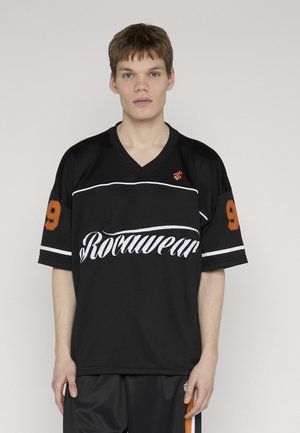 Giovane uomo con capelli castani corti che indossa una maglia sportiva nera con la scritta "Rawwear" e il numero 9 su entrambe le maniche.