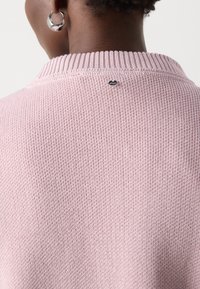 Rosa genser med en teksturert, strikket mønster og ribbestrikket krage. Har en liten logo over kragen og et mykt, lett materiale.