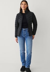 Sort polstret jakke med høj krave og quiltet design. Matchet med blå jeans og sorte ankelstøvler. Enkel, funktionel stil.