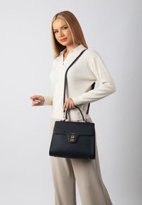 Black leather handbag with a structured design, gold hardware, and a top handle. Features an adjustable shoulder strap and a textured finish.