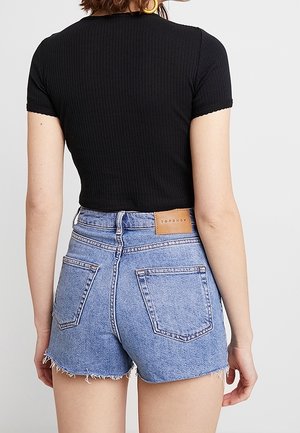 Woman wearing a black ribbed short-sleeve crop top and high-waisted light blue denim shorts with frayed hems.