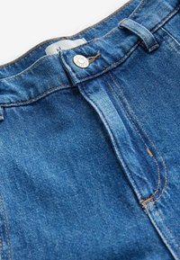 Jean en denim bleu avec bouton métallique et fermeture éclair avant, présentant des coutures orange le long des coutures et de la ceinture.