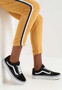 Svarta mockaskorskor med vita detaljer och snören, i kombination med gula korta byxor med svarta och vita sidostrålar.