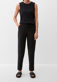 Haut sans manches noir avec épaules texturées, assorti à un pantalon noir à cordon de serrage et des sandales plates noires. Tenue simple et décontractée avec une coupe relaxée.