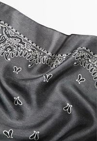 Czarny jedwabny szal z białymi wzorami paisley i kwiatowymi wzdłuż krawędzi, o gładkiej, błyszczącej fakturze i subtelnym układzie.