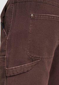 Brune cargo bukser med strukturert stoff, sidelomme og forsterket søm. Fremtredende detaljer inkluderer en metallaccent og et rent design.