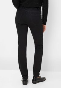 Jean skinny en denim noir avec une texture lisse, design à cinq poches et couture discrète. Portés avec des mocassins noirs brillants.