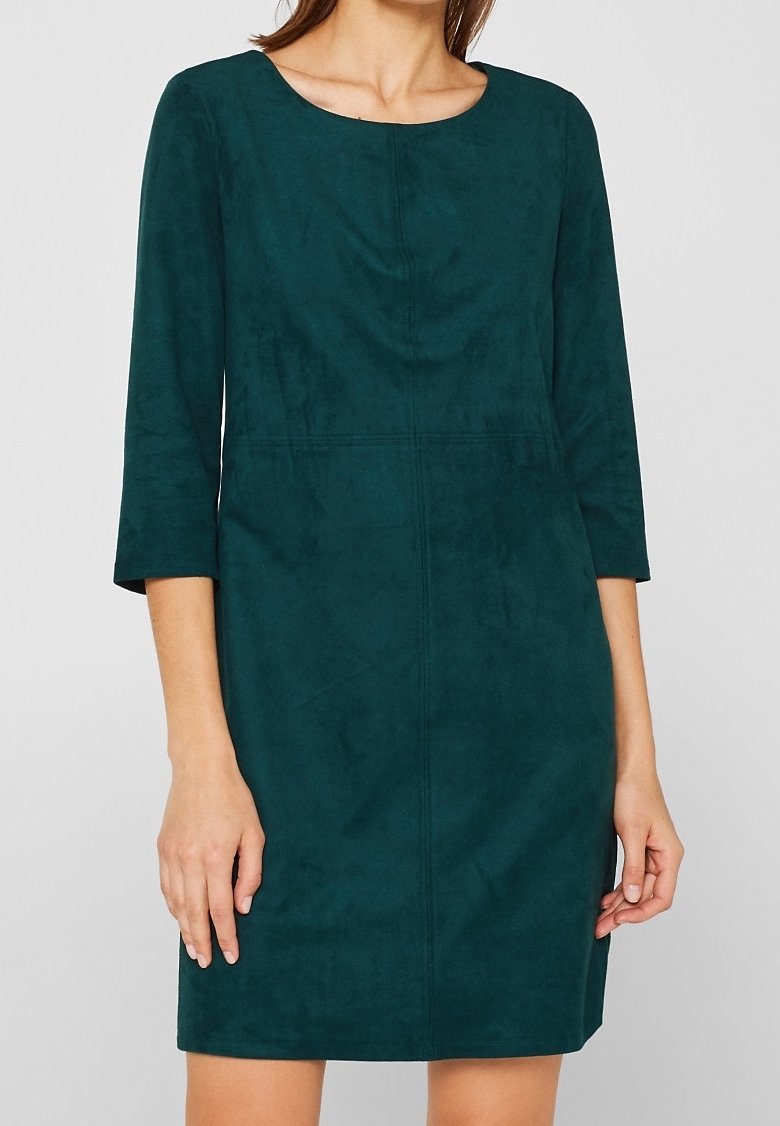 Robe bleu sarcelle en velours jusqu'aux genoux avec des manches trois-quarts et un col rond, portée par une femme avec les bras détendus le long du corps.