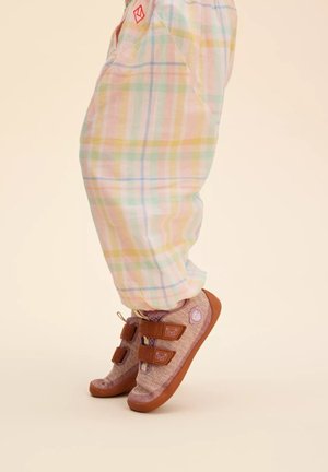 Brightly colored plaid pants feature pastel hues. Footwear is a textured, light purple shoe with brown straps, rubber soles, and a bear logo detail.