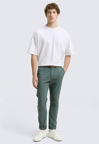Wit katoenen T-shirt met korte mouwen, gecombineerd met groene chino's en witte sneakers. De outfit heeft een eenvoudig, ontspannen ontwerp.