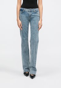 Svetlomodré džínsové nohavice rozšírené dole s mierne vyšším pásom, dizajnom s piatimi vreckami a viditeľnými švami, skombinované s čiernymi podpätkami so špicatou špičkou.