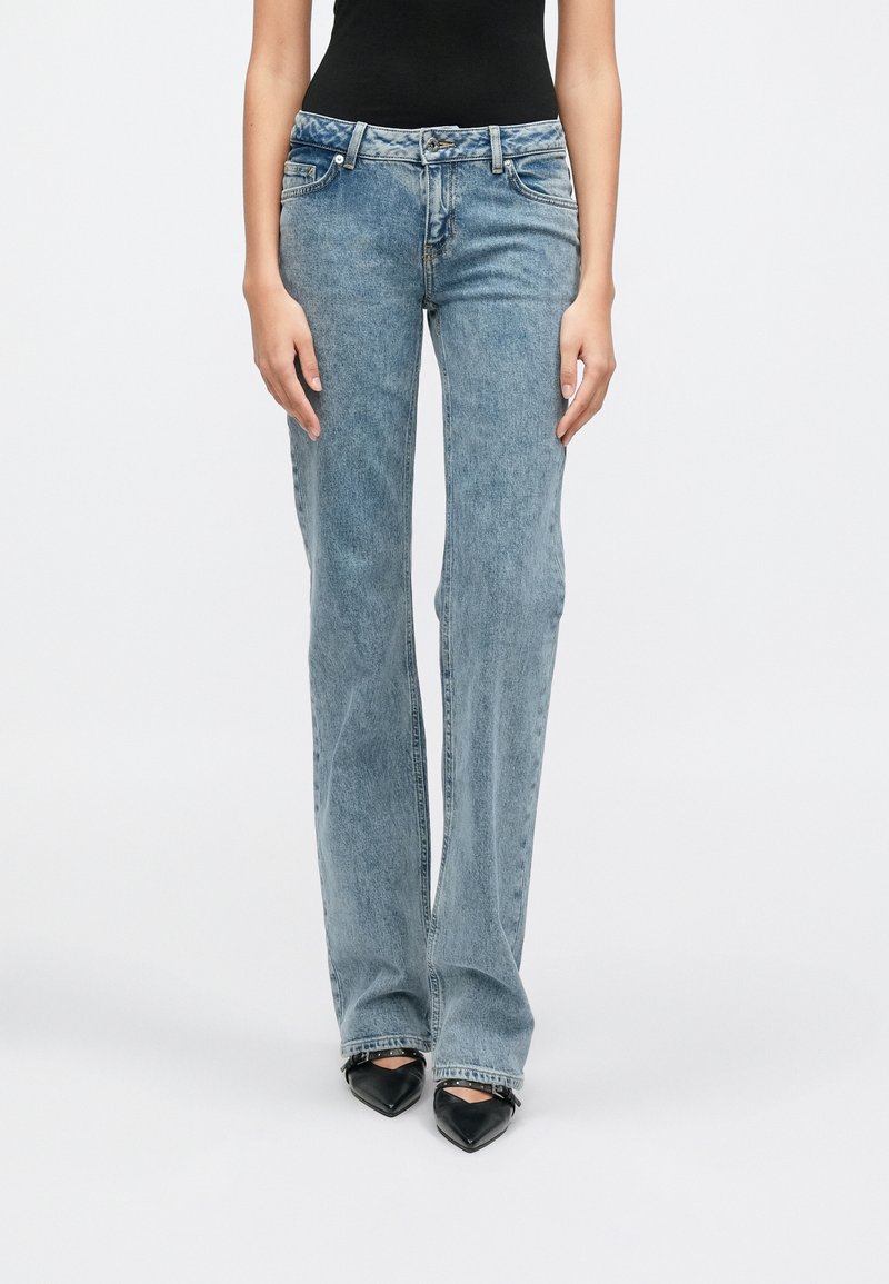 Svetlomodré džínsové nohavice rozšírené dole s mierne vyšším pásom, dizajnom s piatimi vreckami a viditeľnými švami, skombinované s čiernymi podpätkami so špicatou špičkou.