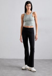 Grå croppet tanktopp med hvit logo, kombinert med svarte utsvingte leggings og beige treningssko. Glatt tekstur og tettsittende design.