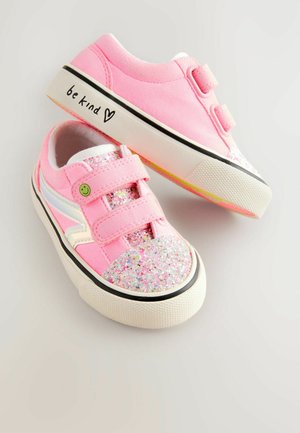 Roza platnena športna obutev z bleščečimi kapicami prstov, dvema Velcro trakovima, črnimi akcenti in napisom "bodi prijazen" na strani.