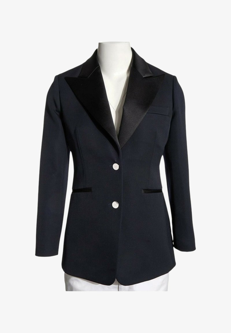 Blazer noir confectionné avec des revers en pointe en satin, deux boutons blancs et des poches passepoilées devant sur un torse de mannequin blanc.