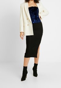 Gonna midi nera a costine con uno spacco laterale, abbinata a un top corsetto in velluto blu navy lucido e a un blazer oversize crema, indossato con stivaletti neri.