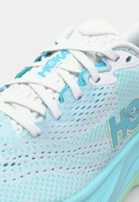 Light blue running shoe with mesh upper, white laces, and Hoka branding. The sole features a slight gradient from light green to blue.