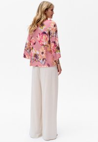 Kwiatowa bluzka z różowego materiału z rękawami 3/4, zestawiona z luźnymi, kremowymi spodniami lnianymi. Charakteryzuje się jaskrawymi wzorami kwiatowymi.