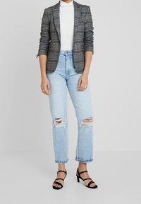 Grå rutig kavaj över en vit polotröja, kombinerad med ljusblå rivna jeans och svarta remsandaletter.