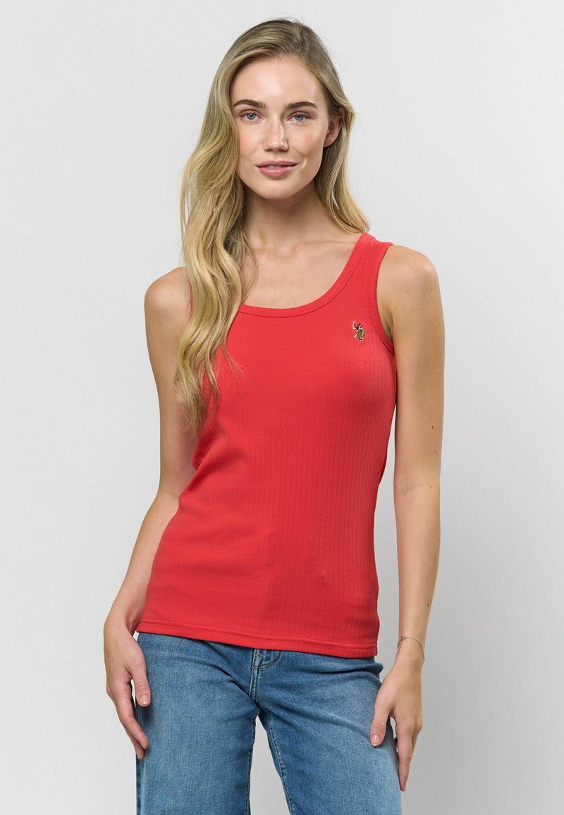 Červený žebrovaný top s kulatým výstřihem a malou vyšitou dekorací, spárovaný s modrými džíny. Model předvádí pohled zepředu.