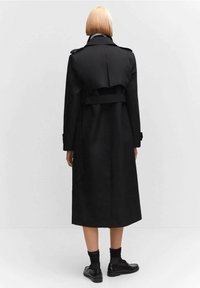 Czarny, długi trencz o dwurzędowym kroju, z paskiem w talii i pagonami na ramionach. Gładka tkanina i dopasowana sylwetka.