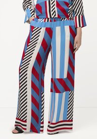 Pantaloni palazzo audaci con una combinazione di righe rosse, blu, nere e bianche e forme geometriche. Realizzati in tessuto leggero con tasche.