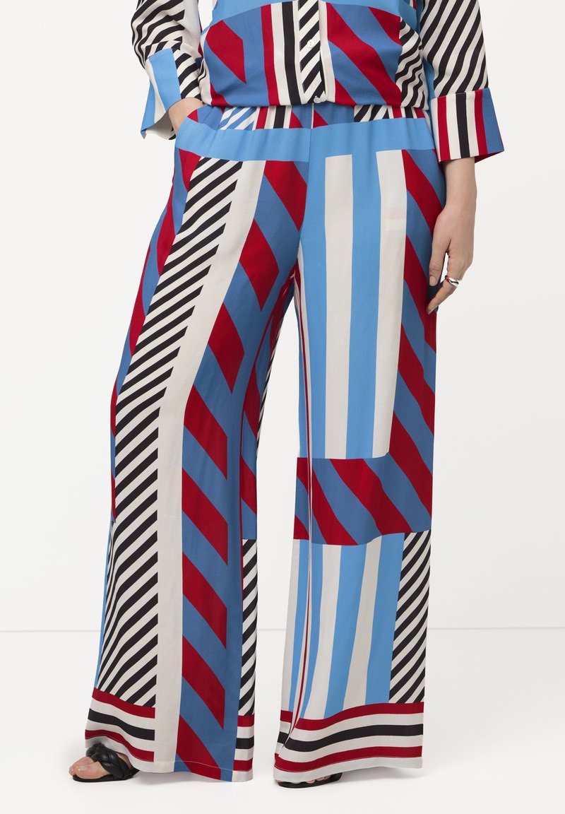 Pantaloni palazzo audaci con una combinazione di righe rosse, blu, nere e bianche e forme geometriche. Realizzati in tessuto leggero con tasche.