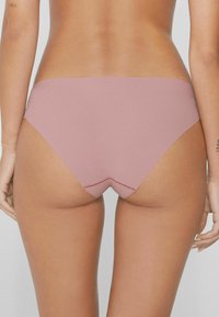 Růžový, bezešvý spodní díl bikiny s hladkým povrchem a nízkým pasem. Má V-švů na zadní straně a minimální krytí.