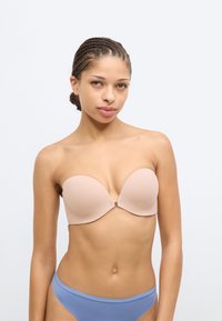 Μπεζ σουτιέν χωρίς τιράντες με λεία υφή και κούμπωμα μπροστά, σε συνδυασμό με ανοιχτό μπλε σλιπ. Απλός σχεδιασμός και ραφές χωρίς ραφές.