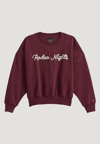 Sweat-shirt bordeaux à manches longues avec texte blanc en cursive "Rodeo Nights" sur le devant et petite broderie jaune sur le poignet gauche.