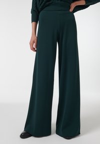Groene wijde broek gemaakt van zachte stof, met een hoge tailleband en een gladde textuur, die tot op de vloer reikt met een ontspannen pasvorm.