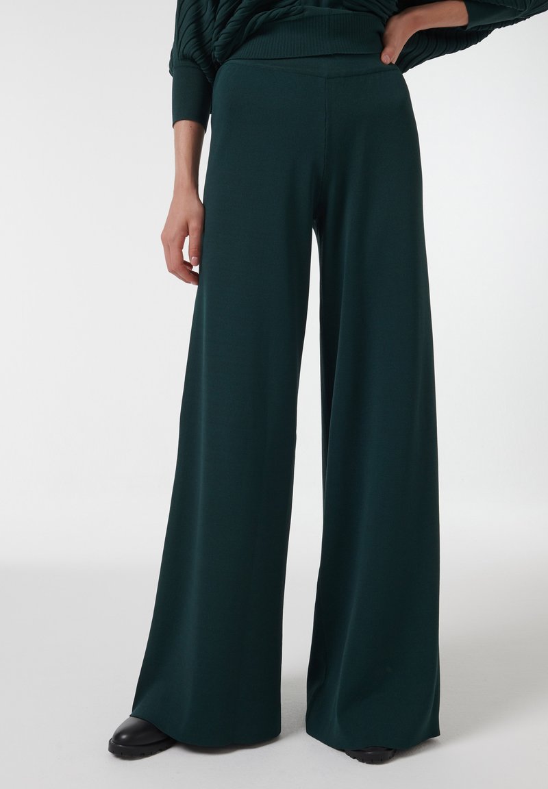 Groene wijde broek gemaakt van zachte stof, met een hoge tailleband en een gladde textuur, die tot op de vloer reikt met een ontspannen pasvorm.